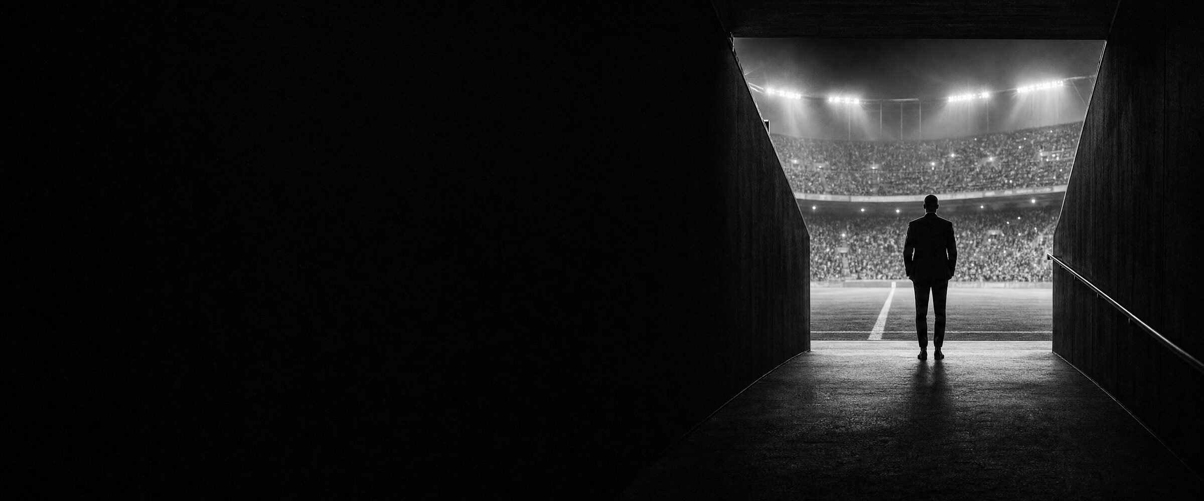 A figure in a suit standing at the mouth of a stadium tunnel